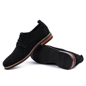 May include: A pair of black suede lace-up shoes with a brown leather trim around the sole.