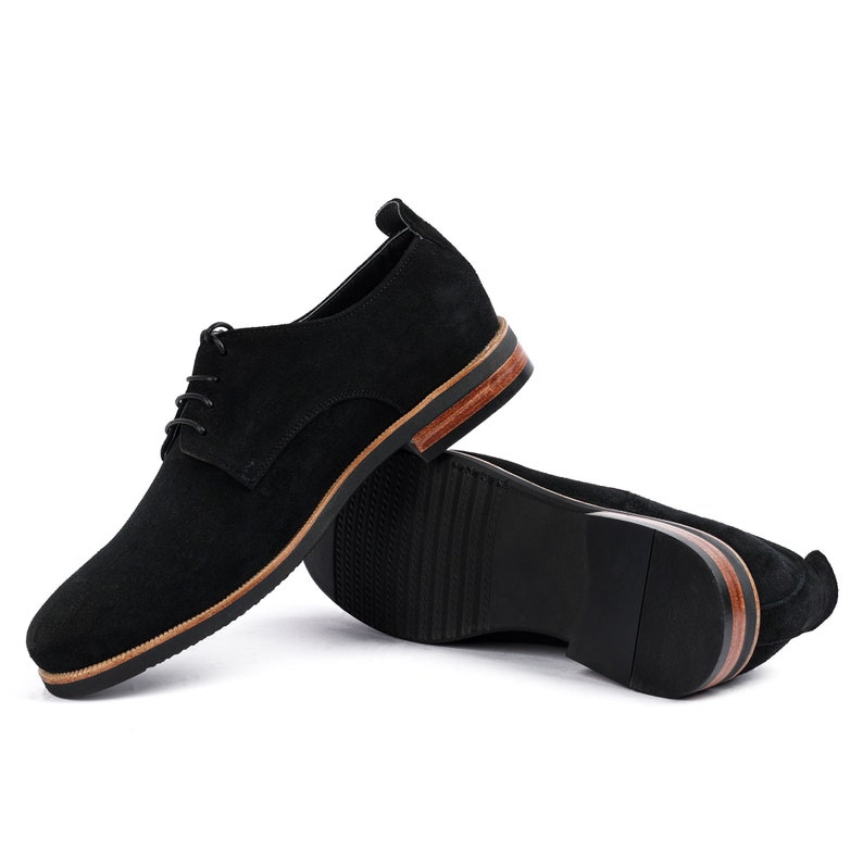 May include: A pair of black suede lace-up shoes with a brown leather trim around the sole.