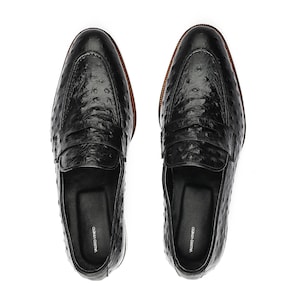 May include: A pair of black leather loafers with an ostrich print. The loafers have a leather sole and a leather lining. The loafers are made by the brand "Valerio Veneto".
