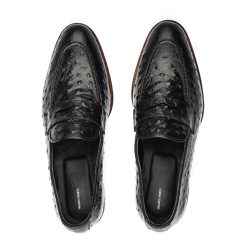 May include: A pair of black leather loafers with an ostrich print. The loafers have a leather sole and a leather lining. The loafers are made by the brand "Valerio Veneto".
