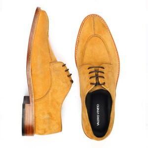 May include: Mustard-coloured suede dress shoes with brown laces. The shoes feature a classic design with a rounded toe and stitched sole. The brand name "VALERIO VENETO" is visible on the insole. The shoes are displayed against a white background.