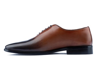 Puede incluir: Un zapato oxford de cuero marrón con suela negra. El zapato tiene un degradado de color de marrón oscuro a marrón claro.