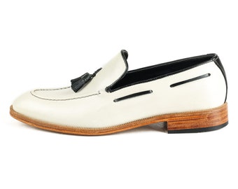May include: White leather loafers with a black tassel and a brown leather sole.