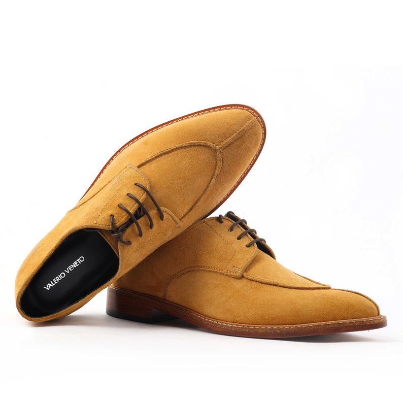 May include: Mustard-coloured suede dress shoes with dark brown laces. The shoes have a classic design with a stitched sole. The brand name "VALERIO VENETO" is printed on the insole.