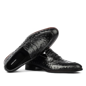May include: Black leather loafers with an ostrich print design. The loafers have a penny strap detail and a brown leather sole. The brand name "Valerio Veneto" is visible on the insole.