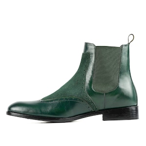 Op de afbeelding: Een paar groene leren enkellaarsjes met een suède neus en een decoratief stikselpatroon. De laarsjes hebben een slip-on ontwerp en een blokhak.