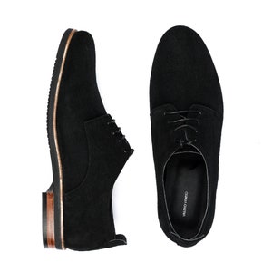 May include: A pair of black suede lace-up shoes with brown leather trim. The shoes have a simple design and are made of high-quality materials.