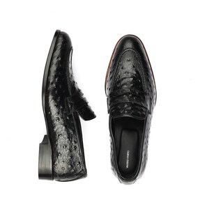 May include: A pair of black leather loafers with an ostrich print. The loafers have a leather sole and a leather lining. The loafers are made by the brand "VALERIO VENEZIA".