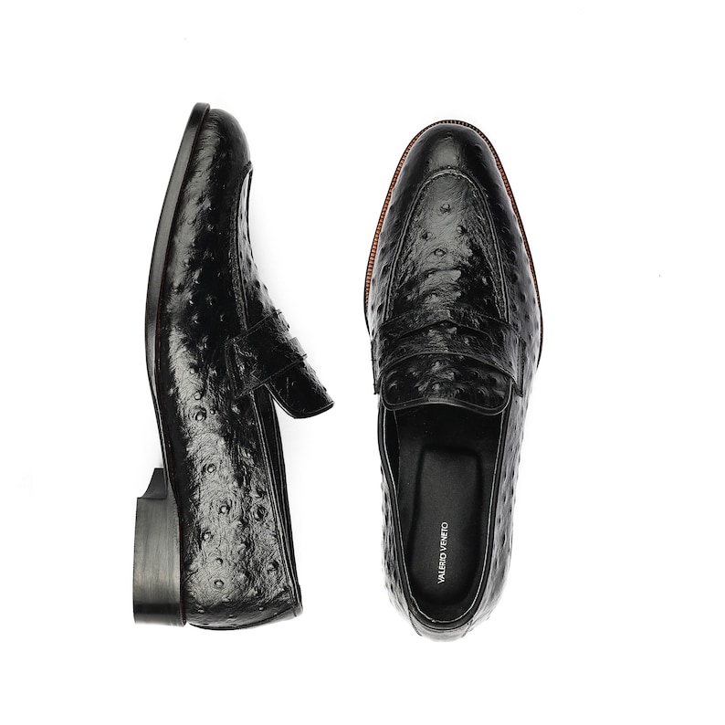May include: A pair of black leather loafers with an ostrich print. The loafers have a leather sole and a leather lining. The loafers are made by the brand "VALERIO VENEZIA".