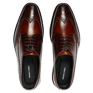 Pu&ograve; includere: Un paio di scarpe da uomo in pelle marrone con design brogue e chiusura con lacci. Le scarpe hanno un design a punta alare e sono realizzate in pelle liscia. Il nome del marchio "VALERIO VENETO" &egrave; stampato all'interno di ogni scarpa.