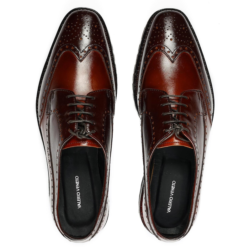 Pu&ograve; includere: Un paio di scarpe da uomo in pelle marrone con design brogue e chiusura con lacci. Le scarpe hanno un design a punta alare e sono realizzate in pelle liscia. Il nome del marchio "VALERIO VENETO" &egrave; stampato all'interno di ogni scarpa.