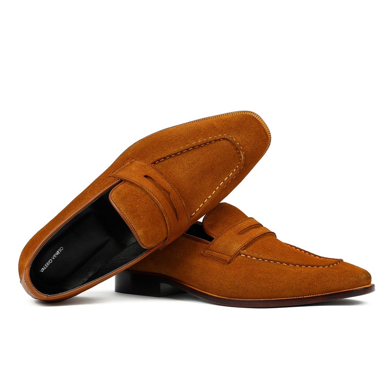 May include: A pair of brown suede loafers with a leather sole. The loafers have a simple design with a single strap across the top. The brand name "VALERO VENETO" is visible on the insole.