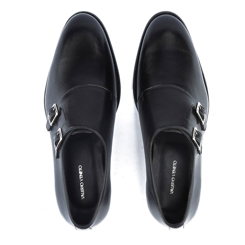 May include: A pair of black leather double monk strap shoes. The shoes have silver-colored buckles and the brand name "VALERIO VENETO" is printed on the insole. The shoes are shown from a top-down perspective.