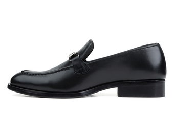 May include: Black leather loafer with a buckle detail. The shoe has a pointed toe and a low heel.