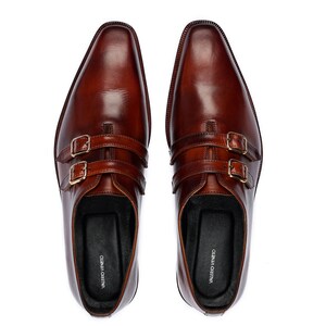 May include: A pair of brown leather double buckle monk strap shoes. The shoes have a pointed toe and are made of a smooth leather. The brand name "VALERIO VENEITO" is printed on the inside of each shoe.