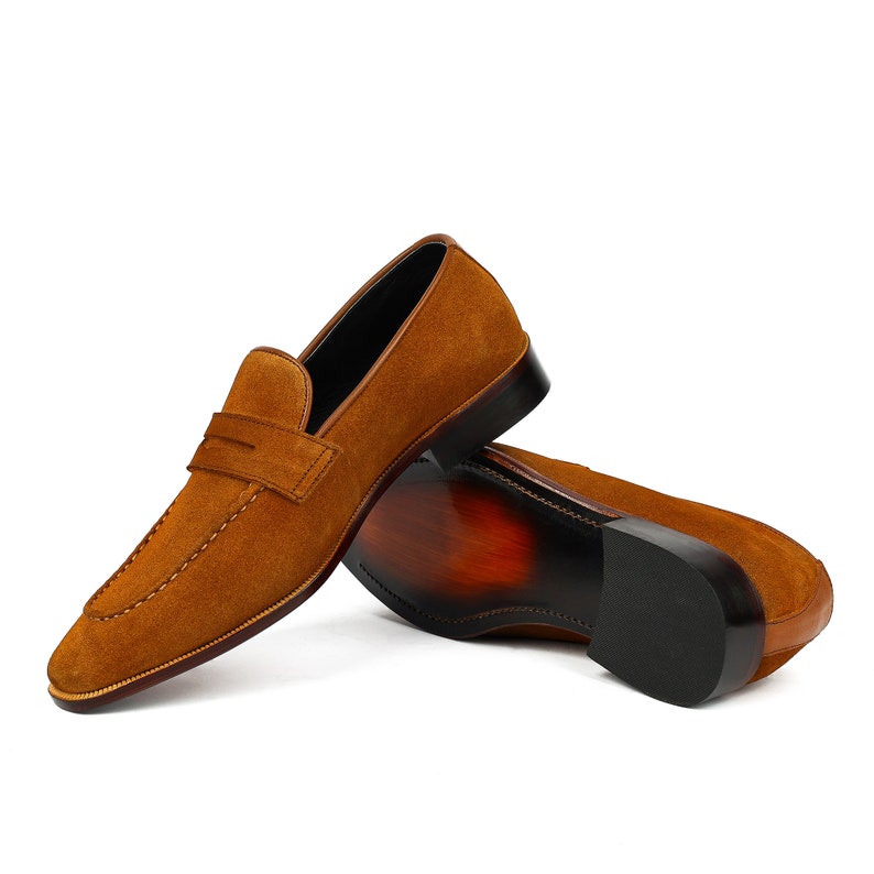 May include: A pair of brown suede loafers with a leather sole. The loafers have a simple design with a single strap across the top.