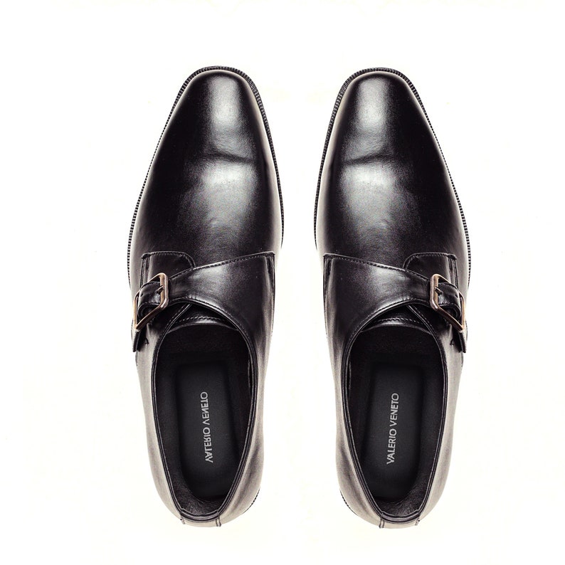 May include: A pair of black leather monk strap shoes with a silver buckle. The shoes have a pointed toe and a low heel. The brand name "VALERIO VENETO" is printed on the inside of each shoe.
