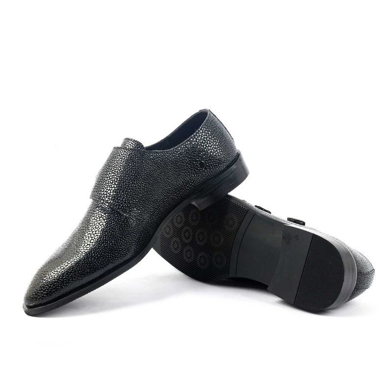 K&ouml;nnte beinhalten: Ein Paar schwarze Lederschuhe mit Schnallenverschluss. Die Schuhe haben eine strukturierte, genarbte Oberfl&auml;che.
