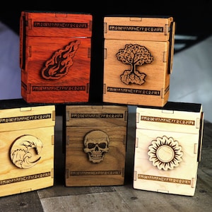 Op de afbeelding: Vijf houten kaartenboxen met verschillende ontwerpen. De dozen zijn gemaakt van verschillende soorten hout en hebben verschillende kleurschakeringen. De ontwerpen zijn een vlam, een boom, een golf, een schedel en een zon.