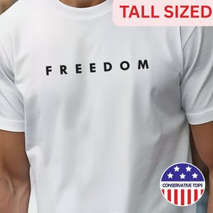 May include: White t-shirt with the word "FREEDOM" printed in black block letters. The shirt has a crew neck and short sleeves. A small graphic with stars and stripes and the words "CONSERVATIVE TOPS" is visible.