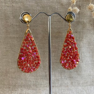 May include: A pair of teardrop-shaped earrings with a gold wire frame and coral-colored beads. The beads are small and square-shaped, creating a textured look.