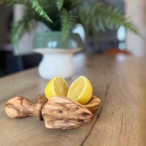Peut inclure: Un presse-agrumes en bois avec un bol et deux moitiés de citron. Le presse-agrumes est en bois d'olivier et présente un grain naturel texturé. Les citrons sont jaune vif et le bol est également en bois d'olivier. La scène se déroule sur une surface en bois.