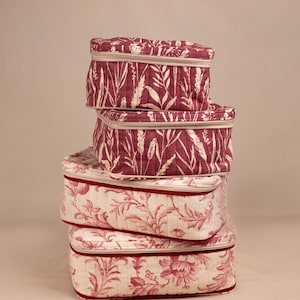 May include: A stack of four rectangular quilted storage cases with zippered closures. The top two cases feature a dark red fabric with a white botanical wheat pattern, while the bottom two cases feature a cream fabric with a red floral print.