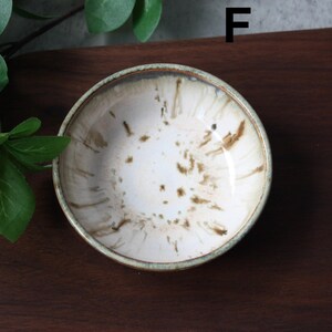 May include: A small, round ceramic bowl with a white interior and brown speckled design. The rim has a light green and brown border. The bowl is likely used for serving small portions of food or as a decorative piece.
