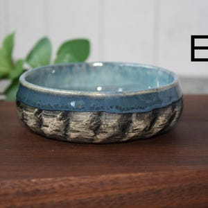 May include: A set of three ceramic mugs with a speckled, matte finish. The mugs are in shades of cream, light gray, and dark gray. Each mug has a simple, minimalist design and a rounded handle.