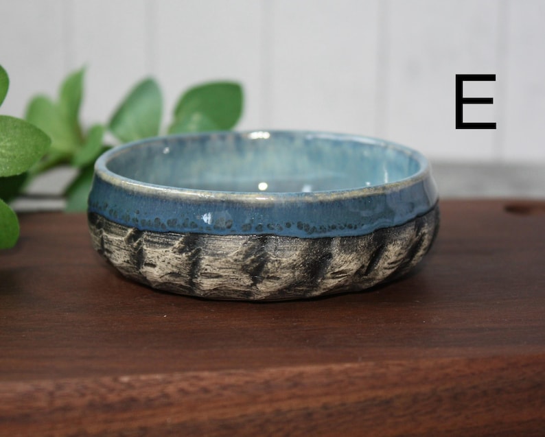 May include: A set of three ceramic mugs with a speckled, matte finish. The mugs are in shades of cream, light gray, and dark gray. Each mug has a simple, minimalist design and a rounded handle.