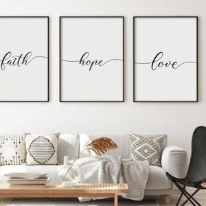 Puede incluir: Tres impresiones enmarcadas en negro con fondos blancos y caligrafía negra. Las impresiones dicen "fe", "esperanza" y "amor". Las impresiones están colgadas en una pared blanca sobre un sofá blanco con almohadas de patrones blanco y negro.