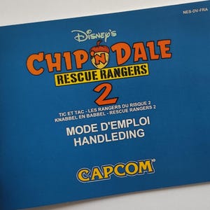 Peut inclure: Manuel d'instructions bleu pour le jeu NES Chip 'n Dale Rescue Rangers 2. La couverture présente le titre en jaune et orange avec une image de dessin animé de Chip et Dale. Le manuel est pour la version française du jeu.