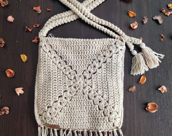 May include: A beige crochet bag with a heart-shaped strap. The bag features a floral design and fringe along the bottom. The bag has a tag that says "MARcrochet".