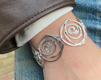 May include: A silver-toned bracelet featuring multiple circular links, each containing an intricate, swirling spiral design with small, embossed oval details along the outer edges of the metal frames.