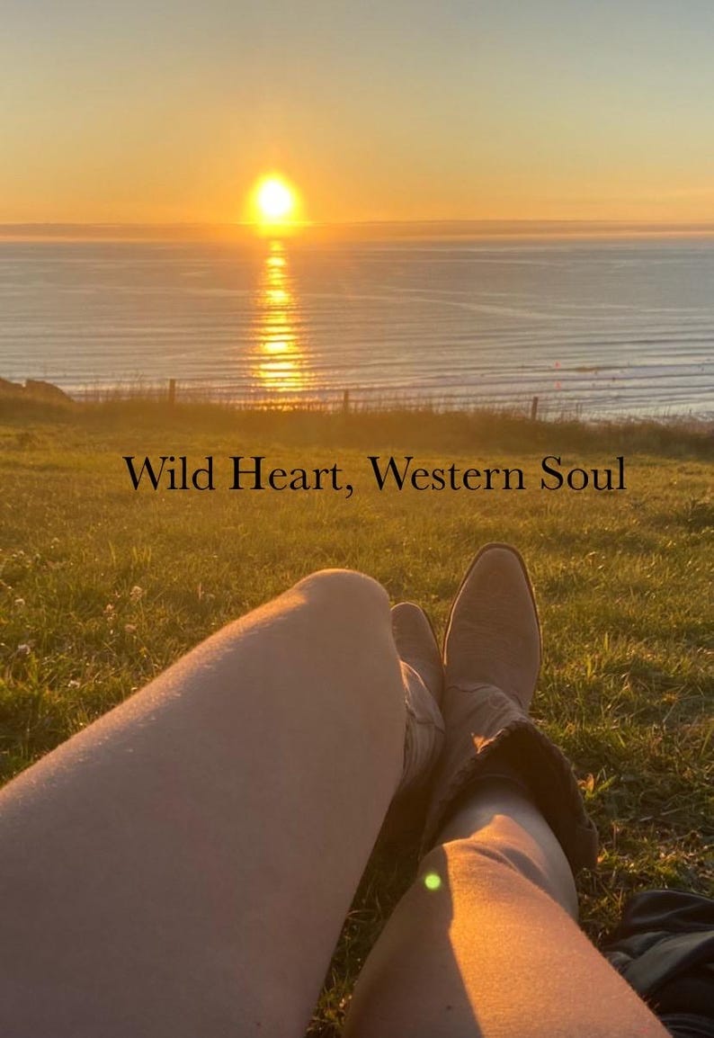 Pode incluir: Um par de botas de couro castanho-claro em estilo western cal&ccedil;adas nas pernas, posicionadas contra um p&ocirc;r do sol sobre o oceano. O texto "Wild Heart, Western Soul" est&aacute; centralizado no meio da imagem, sobrepondo a paisagem relvada.