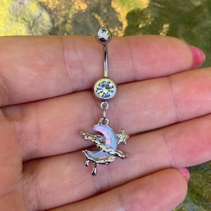 Könnte beinhalten: Ein silberfarbener Bauchnabelpiercing mit einem gebogenen Stab, der oben und unten mit einem klaren, runden Kristall besetzt ist. Ein Anhänger in Form eines Mondsichelelements mit irisierender Oberfläche und kleinem Stern hängt unten.