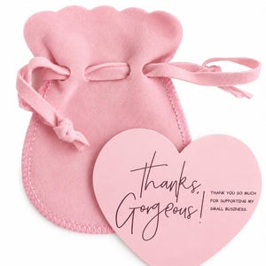 Pode incluir: Uma bolsa de joias de veludo rosa claro com cord&atilde;o e borda superior recortada, acompanhada por um cart&atilde;o rosa claro em forma de cora&ccedil;&atilde;o com o texto escuro "thanks, Gorgeous!" e "THANK YOU SO MUCH FOR SUPPORTING MY SMALL BUSINESS."