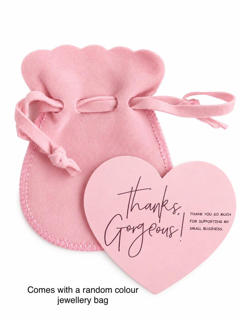 Pode incluir: Uma bolsa de joias de veludo rosa claro com cord&atilde;o e borda superior recortada, acompanhada por um cart&atilde;o rosa claro em forma de cora&ccedil;&atilde;o com o texto escuro "thanks, Gorgeous!" e "THANK YOU SO MUCH FOR SUPPORTING MY SMALL BUSINESS."