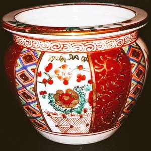 Pode incluir: Um vaso decorativo de cerâmica com formato largo e redondo. O exterior apresenta padrões florais e geométricos vermelhos, dourados, azuis e verdes. A borda tem uma borda dourada.