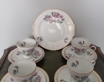 May include: A vintage tea set featuring white porcelain cups, saucers, and a serving plate. Each piece is adorned with a floral pattern in pink, blue, and green, accented with gold trim. The set includes four cups, saucers, and a serving plate.