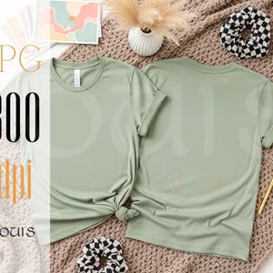 K&ouml;nnte beinhalten: Zwei salbeigr&uuml;ne T-Shirts, eines mit Knoten, werden auf einer strukturierten Oberfl&auml;che pr&auml;sentiert. Das Bild enth&auml;lt ein Scrunchie, Schreibwaren und dekorative Elemente. Der Text "JPG 300 dpi" und der Markenname "LOUIS MOCKUPS" sind ebenfalls sichtbar.