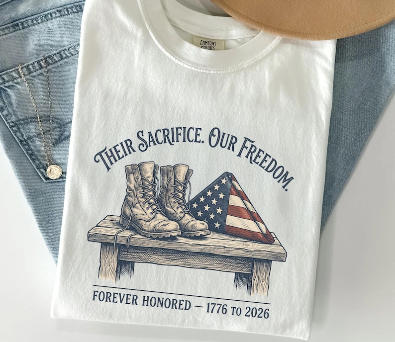 May include: White t-shirt with the text "Their Sacrifice. Our Freedom." and an illustration of combat boots and a folded American flag. The text "Forever Honored - 1776 to 2026" is printed below the illustration.