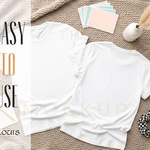 K&ouml;nnte beinhalten: Zwei schlichte, wei&szlig;e T-Shirts mit Rundhalsausschnitt liegen auf einer strukturierten Oberfl&auml;che. Der Text "EASY TO USE" ist sichtbar. Weitere Elemente sind ein Scrunchie, Karten und eine kleine Vase. Mockup-Bild.