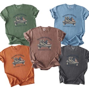 May include: Five different colored t-shirts are displayed, each featuring a graphic of combat boots, an American flag, and the text "Their Sacrifice Our Freedom" and "Forever Honored - 9/11 in 2001". The shirts are in shades of green, blue, brown, orange, and gray.