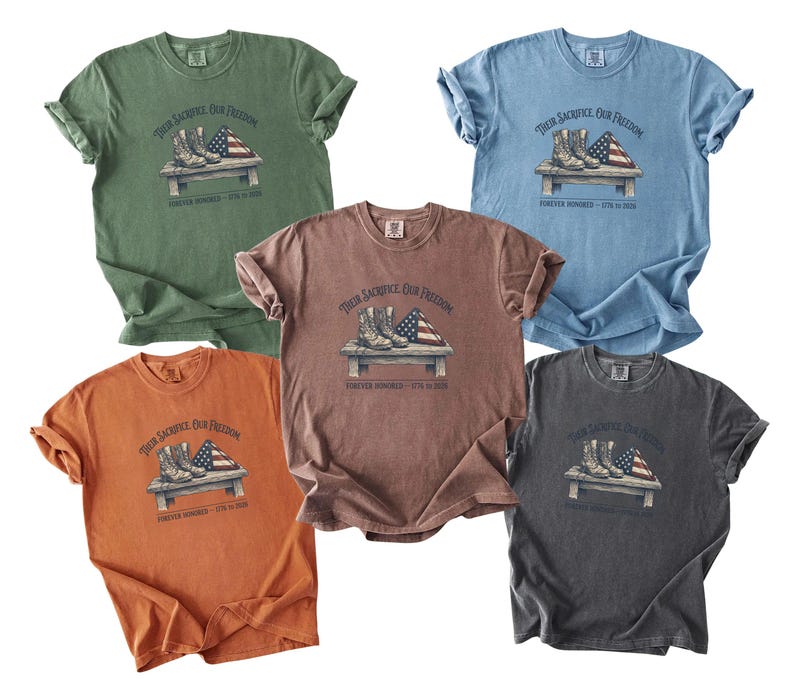 May include: Five different colored t-shirts are displayed, each featuring a graphic of combat boots, an American flag, and the text "Their Sacrifice Our Freedom" and "Forever Honored - 9/11 in 2001". The shirts are in shades of green, blue, brown, orange, and gray.
