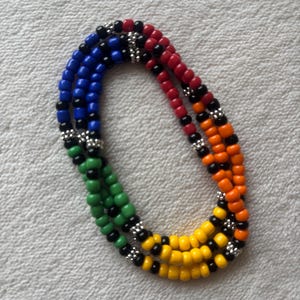 May include: A multi-strand beaded necklace featuring vibrant red, orange, yellow, green, and blue plastic beads arranged in color-blocked sections. Each color segment is separated by small, textured silver-toned metal spacer beads.