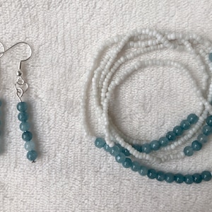 May include: A set of blue and white beaded earrings and a matching beaded necklace. The earrings are silver and have a hook closure. The necklace is made of small white beads and larger blue beads.