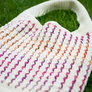 May include: A white crocheted tote bag with pink, orange, and brown stripes. The bag has a wide, flat handle.