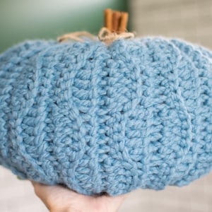 May include: A blue knitted pumpkin with a textured surface. The pumpkin is made of yarn and has a rustic, handmade look.