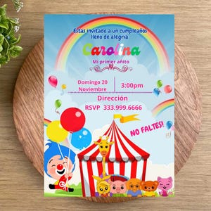 Può includere: Un invito di compleanno colorato a tema circo. L'invito presenta un arcobaleno, palloncini e personaggi dei cartoni animati. Il testo include "Carolina", "Mi primer añito", data, ora e informazioni RSVP.
